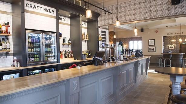 A bar area with a craft beer section, a refrigerated display, and a seating area with a round table and chairs. - Royal Hotel By Greene King Inns (Scunthorpe)