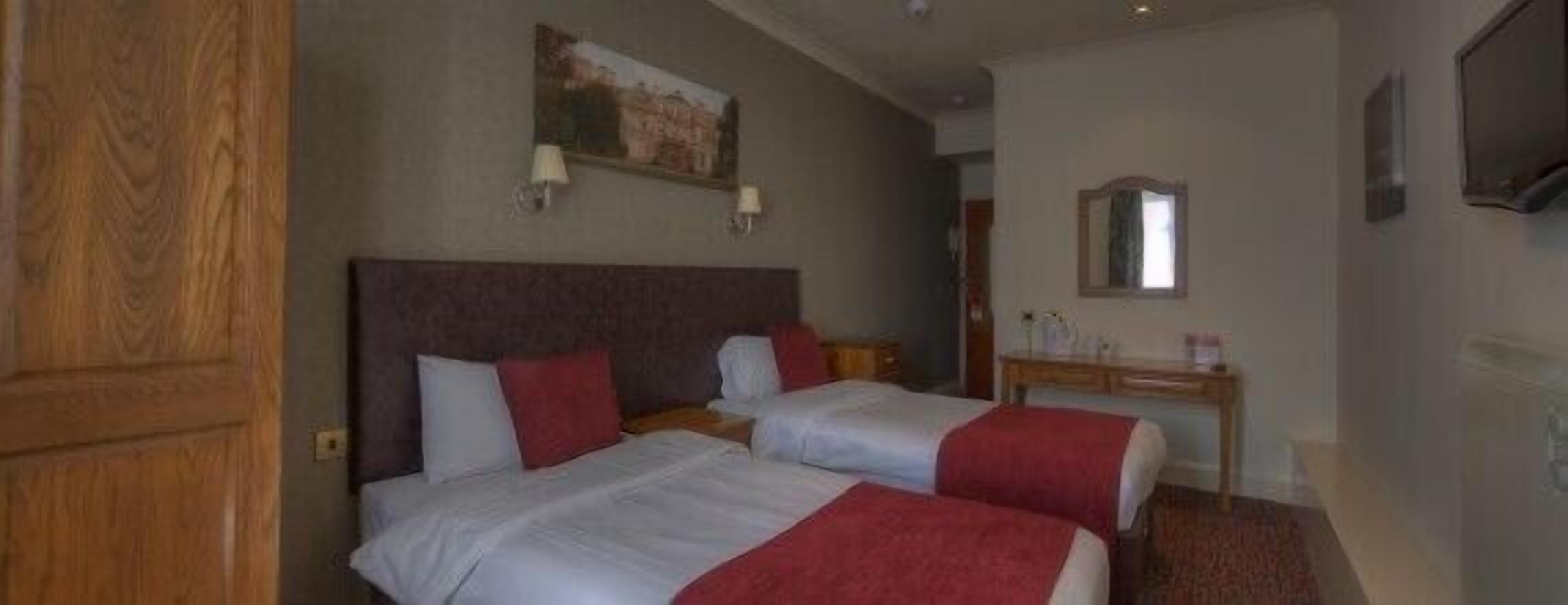 A hotel room with two beds, a wooden wardrobe, a desk with a mirror, and a painting on the wall.