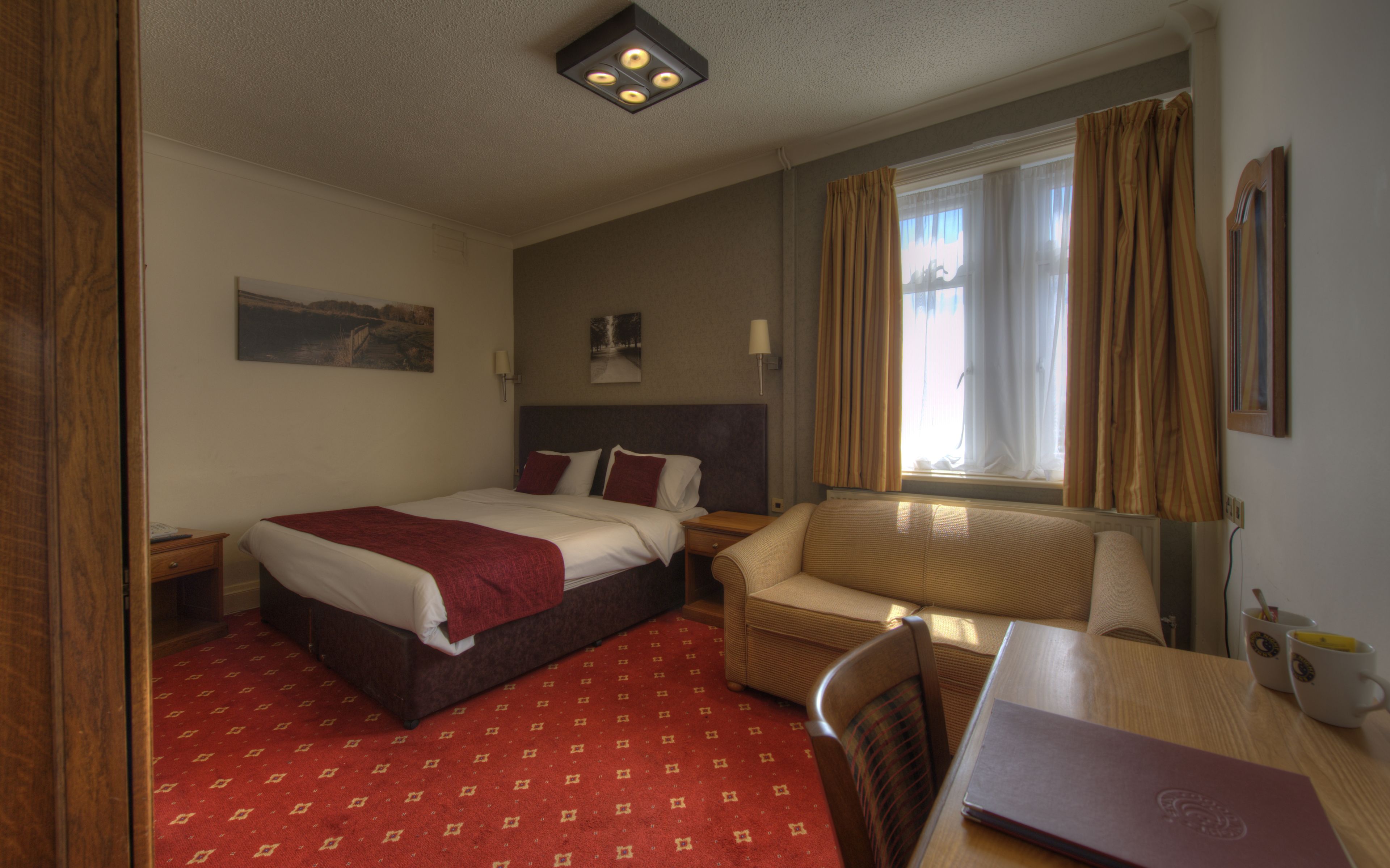 A hotel room with a bed, a sofa, a desk, and a window with curtains.