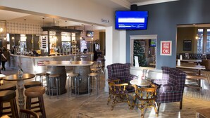 A bar area with stools, a television mounted on the wall, and a Christmas tree in the background. - Royal Hotel By Greene King Inns (Scunthorpe)
