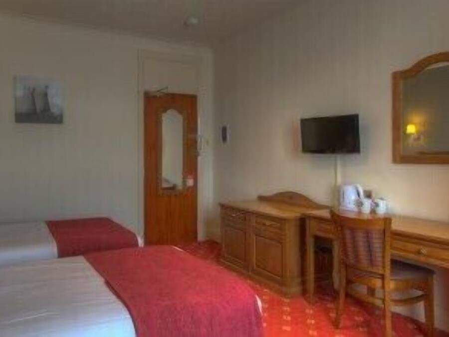 A hotel room with two beds, a desk, a chair, a television, and a mirror.
