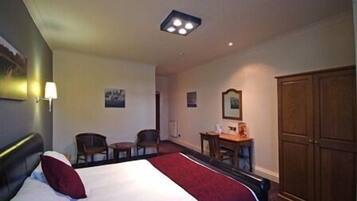A hotel room with a bed, a desk, two chairs, a wardrobe, and a ceiling light fixture.