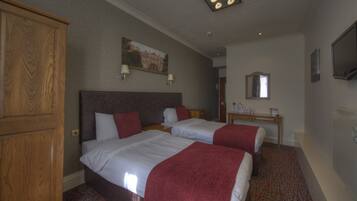A hotel room with two beds, a wooden wardrobe, a desk with a mirror, and a painting on the wall.