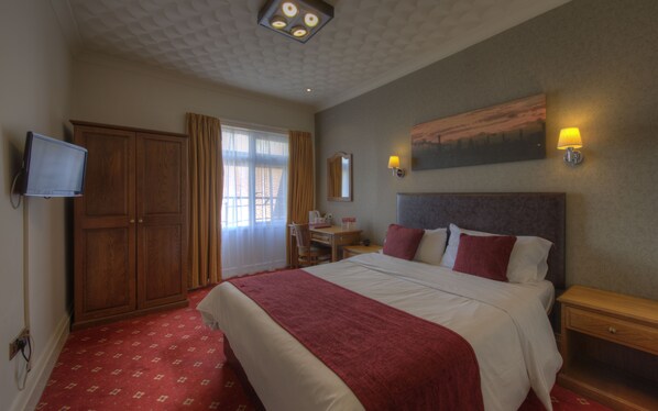 A hotel room with a large bed, a desk, a chair, a television, and a painting on the wall.