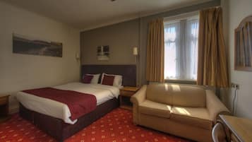 A hotel room with a bed, a sofa, a window with curtains, a lamp, and a painting on the wall.