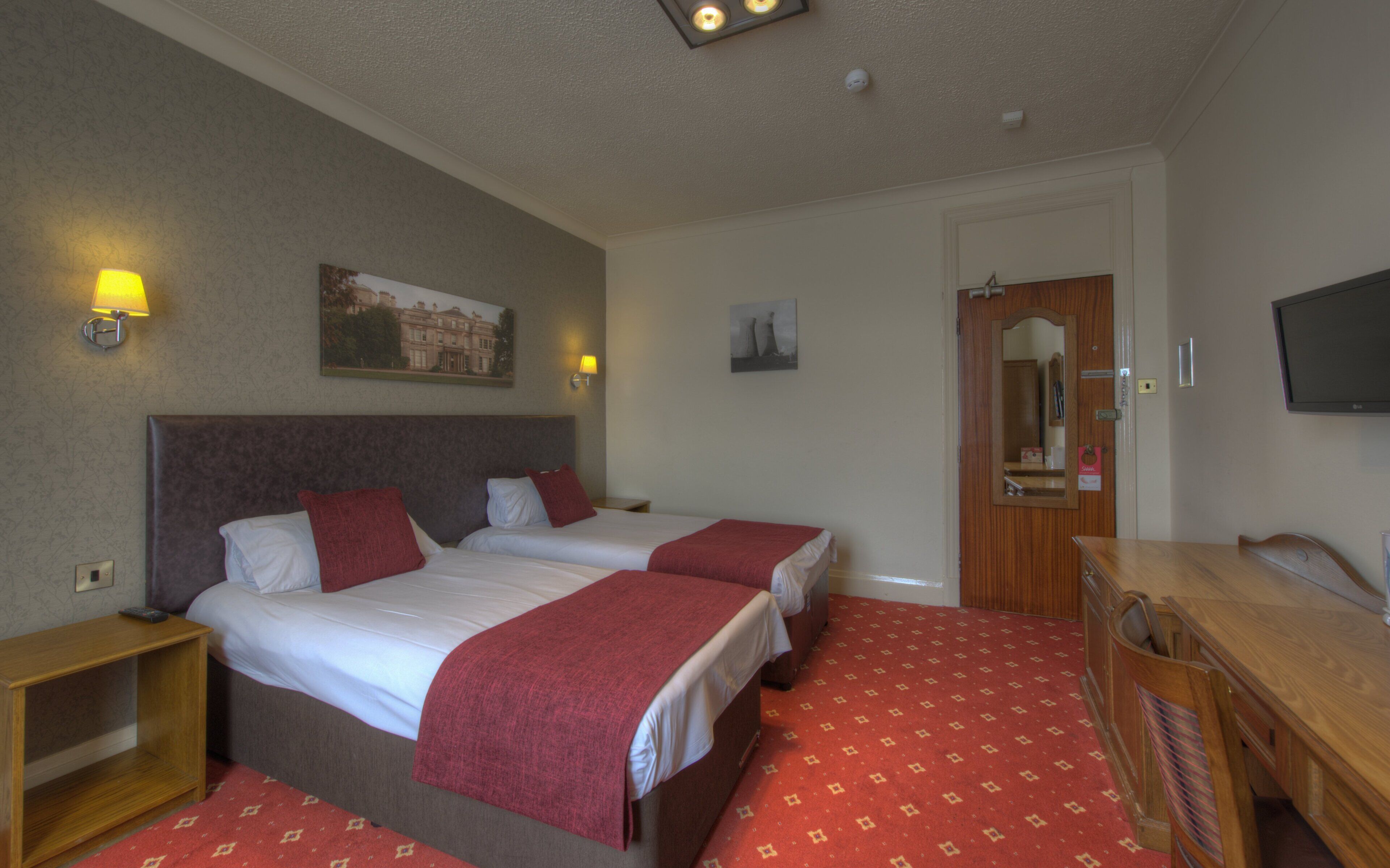 A hotel room with two beds, a wooden dresser, a TV, and a door leading to a bathroom.