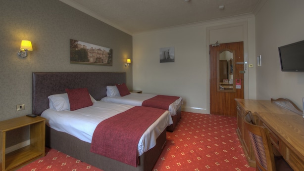 A hotel room with two beds, a wooden dresser, a TV, and a door leading to a bathroom. - Royal Hotel By Greene King Inns (Scunthorpe)