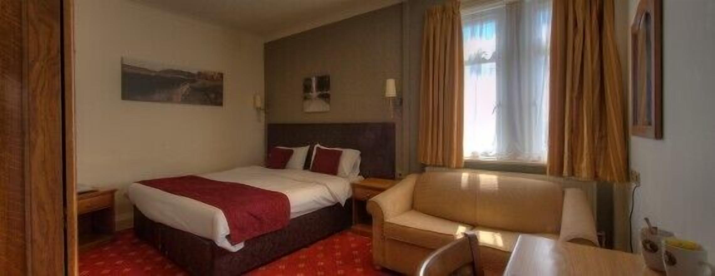 Une chambre d’hôtel avec un lit, une chaise, un bureau et une fenêtre avec des rideaux.