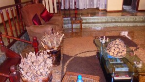 Uma sala de estar com um sofá marrom, uma mesa de centro de vidro e um vaso com flores secas.