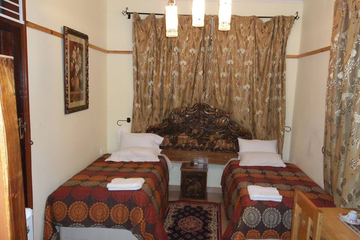 A room with two beds, a wooden headboard, a small table, and a patterned rug.