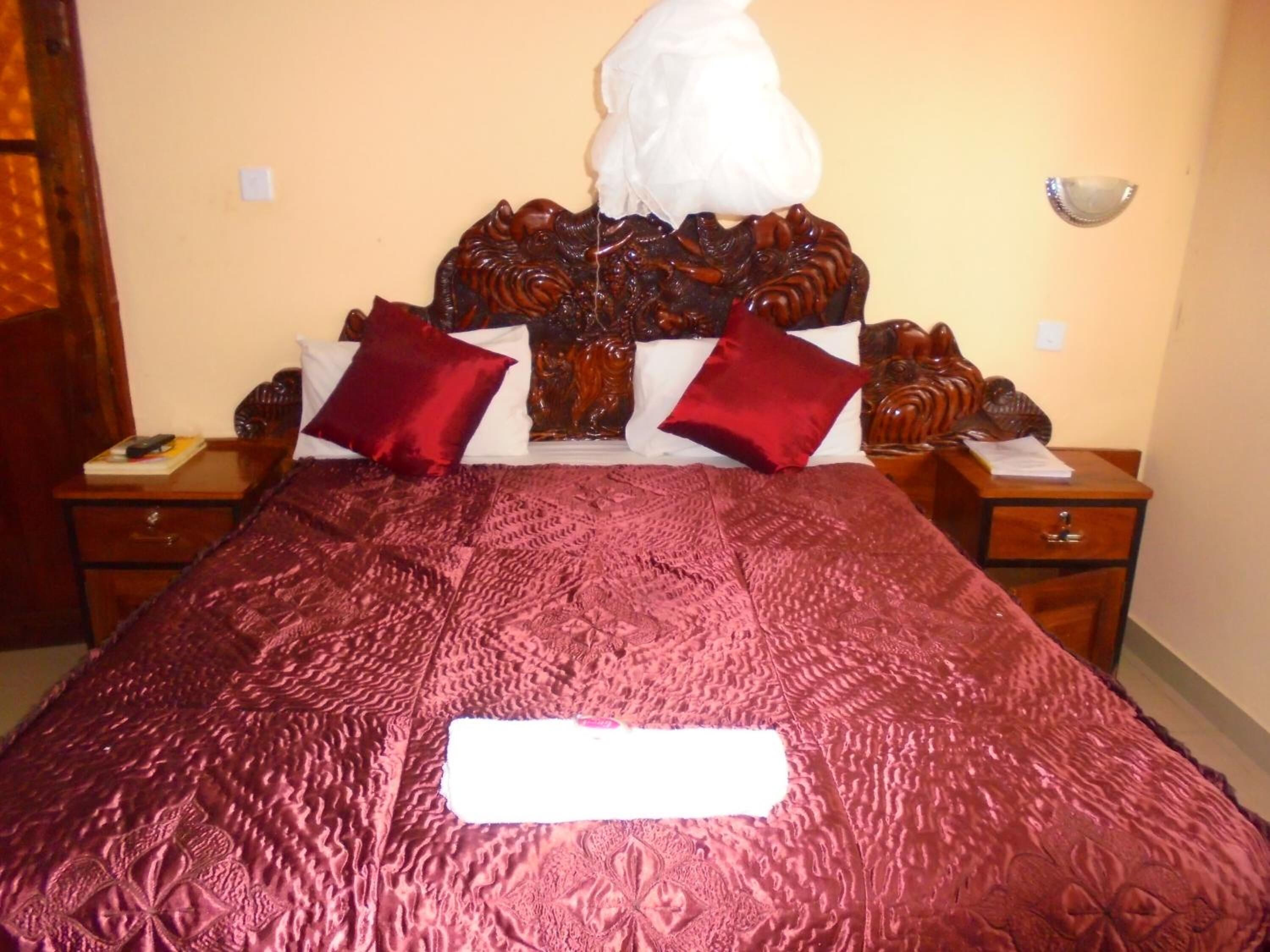 Un lit bien fait, recouvert d’une couvre-lit à motifs rouges, avec deux tables de chevet en bois et un coussin décoratif blanc posé sur la tête de lit.