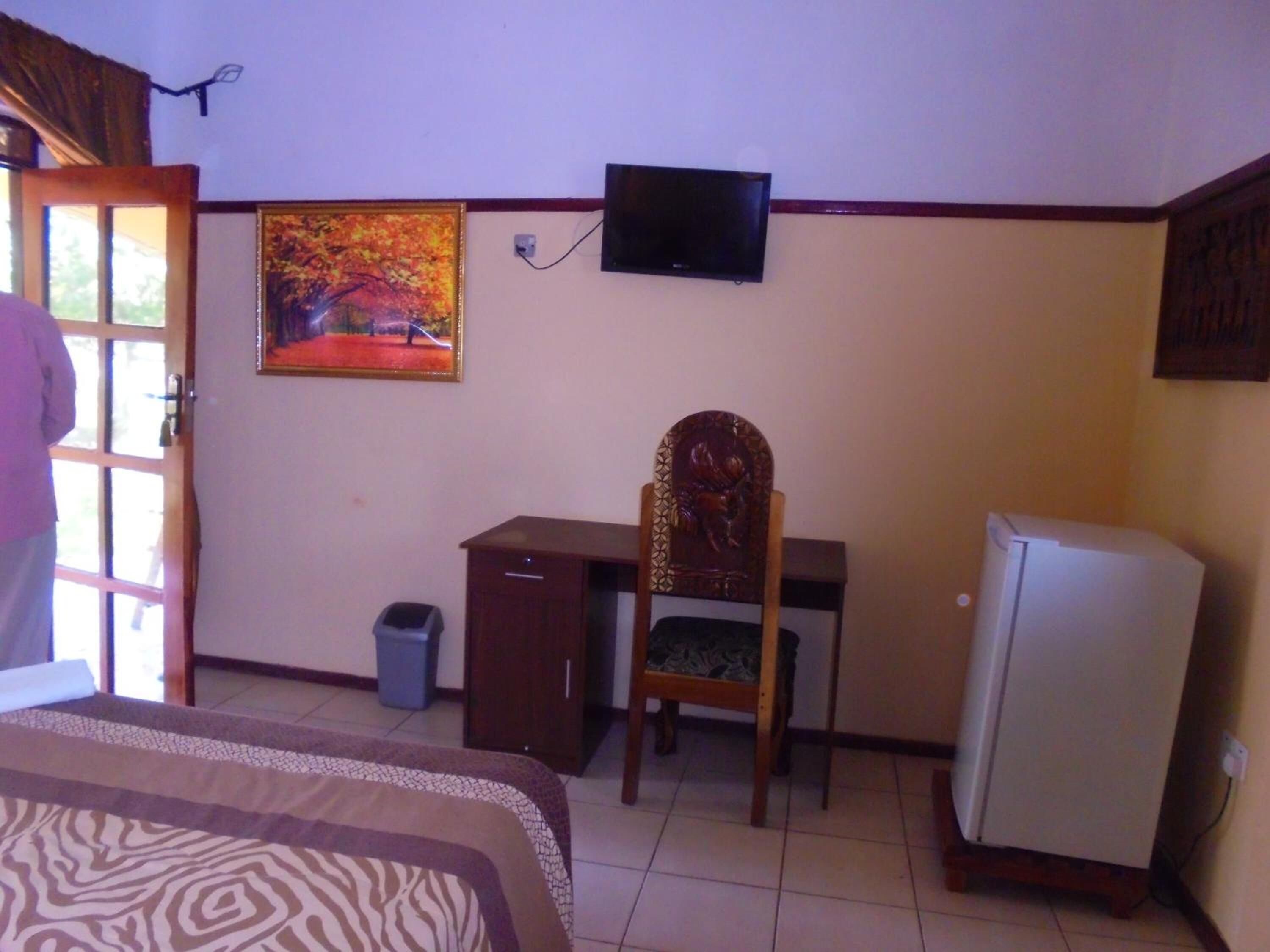 A bedroom with a bed, a desk, a chair, a television, and a refrigerator.
