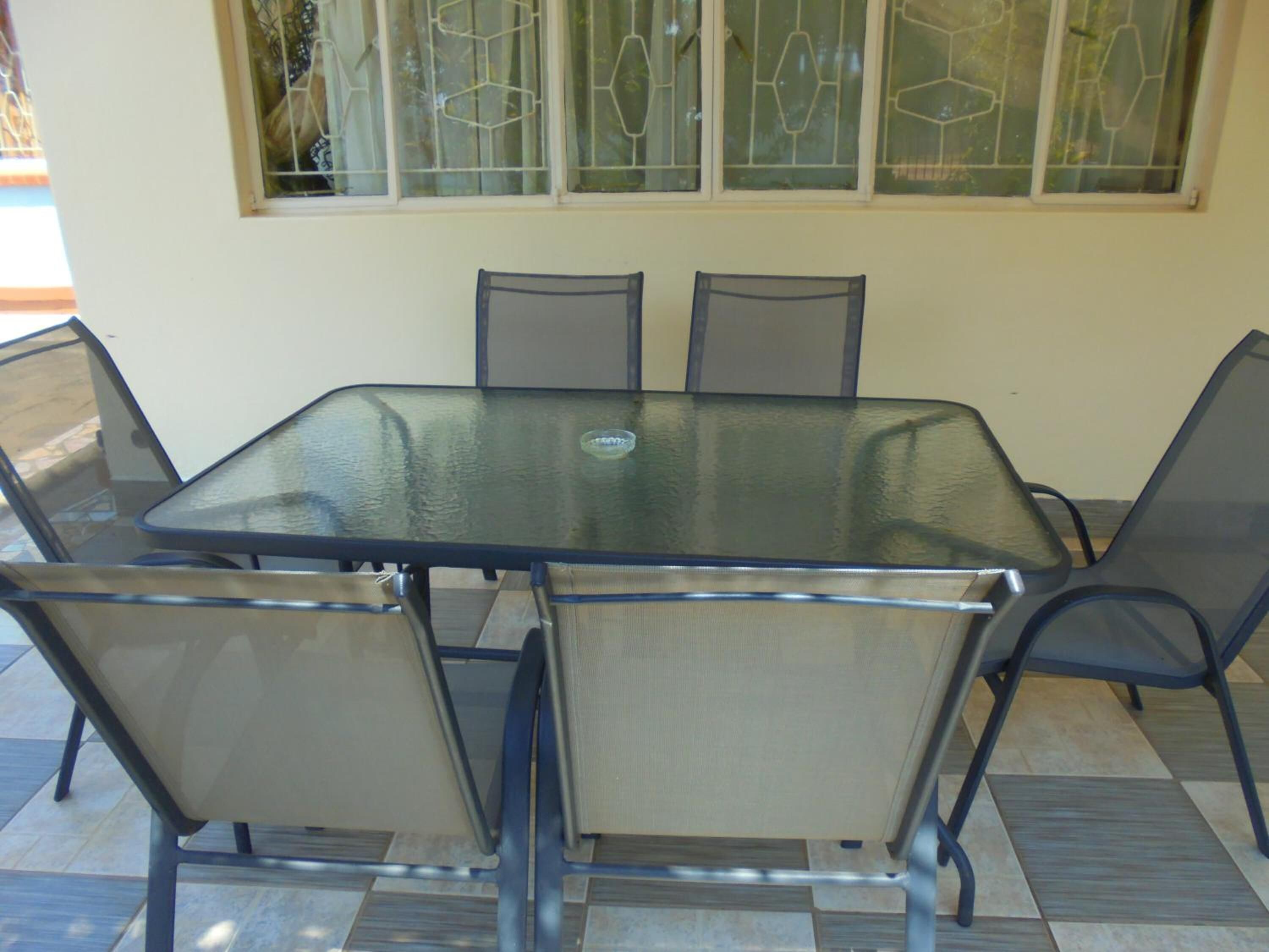 A glass-top table with six chairs, a window with decorative glass panes, and a tiled floor.