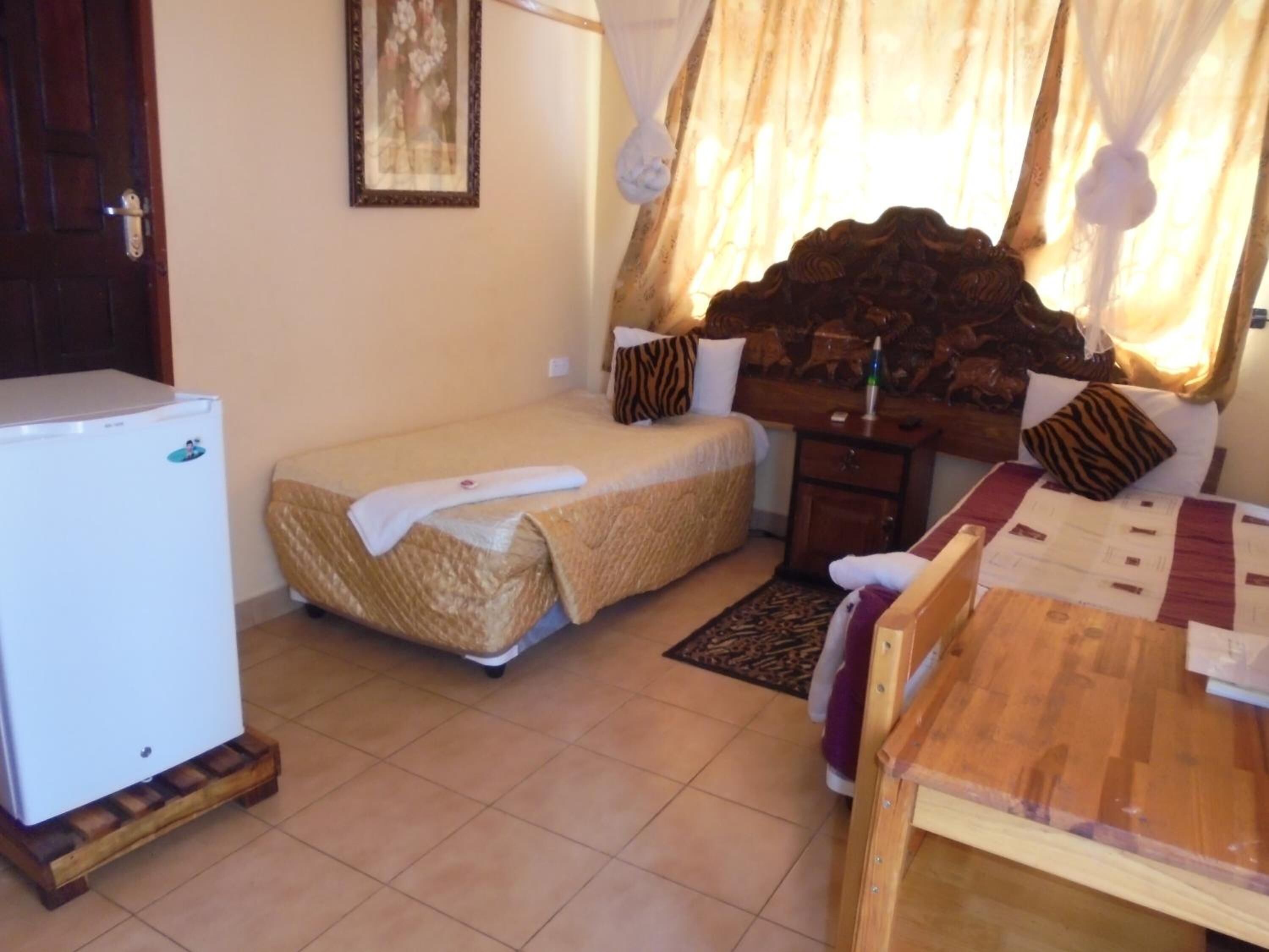 A small hotel room with a bed, a desk, a chair, a refrigerator, and a window with curtains.