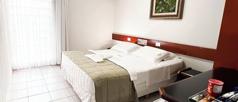 Habitación de hotel con cama, escritorio con computadora, aire acondicionado y un cuadro en la pared.