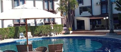 Un área de piscina con sillones de descanso y sombrillas, rodeada de edificios con aires acondicionados.