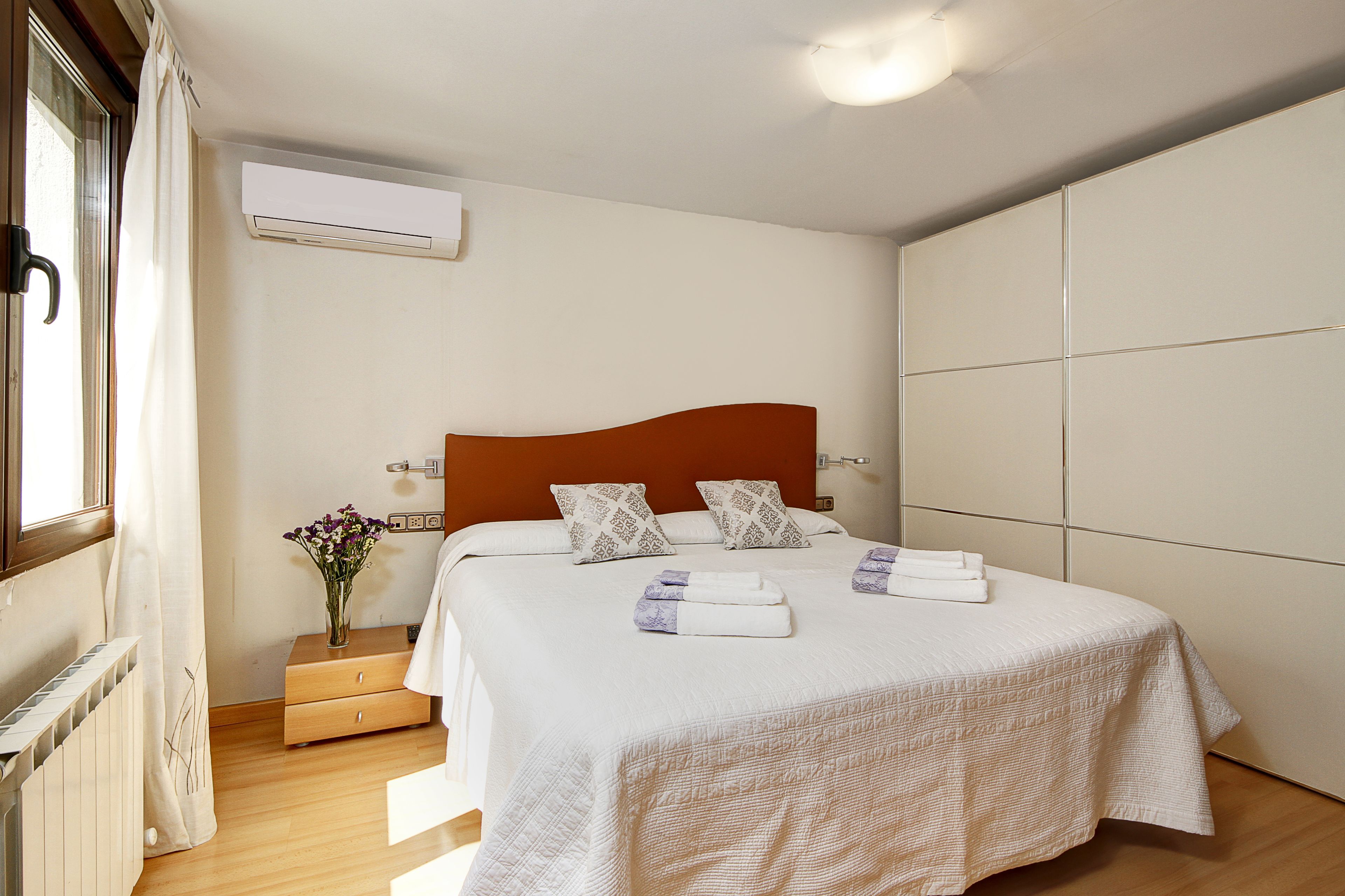 A hotel room with a bed, a nightstand, a dresser, and an air conditioning unit.
