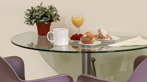 A glass-top table with a potted plant, a white mug, a glass of orange juice, a plate with raspberries, a muffin, and a napkin. - Apartamentos Turísticos Centro (Granada)