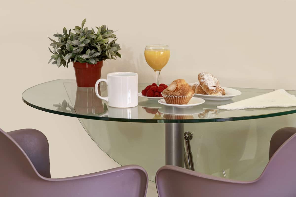 A glass-top table with a potted plant, a white mug, a glass of orange juice, a plate with raspberries, a muffin, and a napkin.