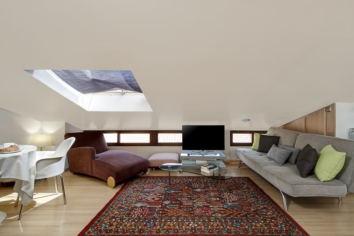 A modern living room with a sofa, a coffee table, a TV, and a patterned rug.