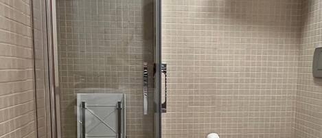 A bathroom with a glass-enclosed shower, a toilet, and a towel rack with folded towels.