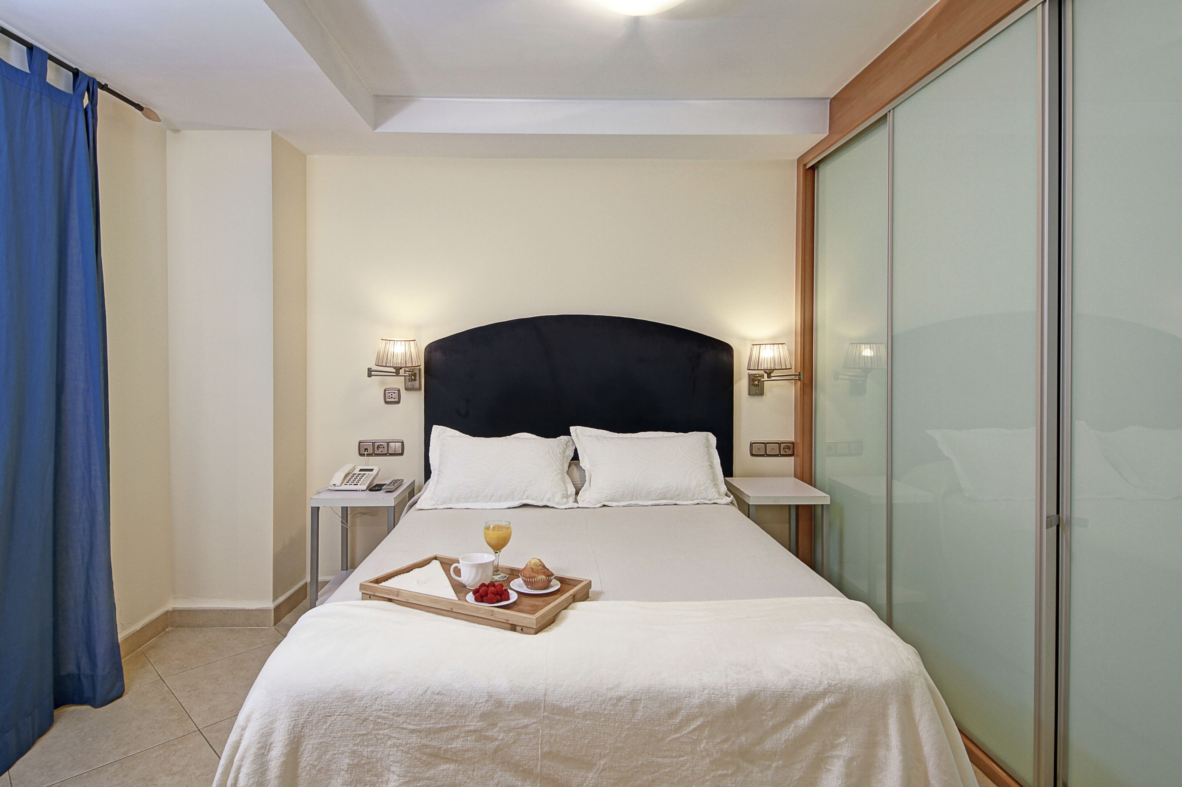 Une chambre d’hôtel avec un grand lit, des lampes de chevet, un téléphone sur la table de chevet et un plateau avec des articles pour le petit-déjeuner.