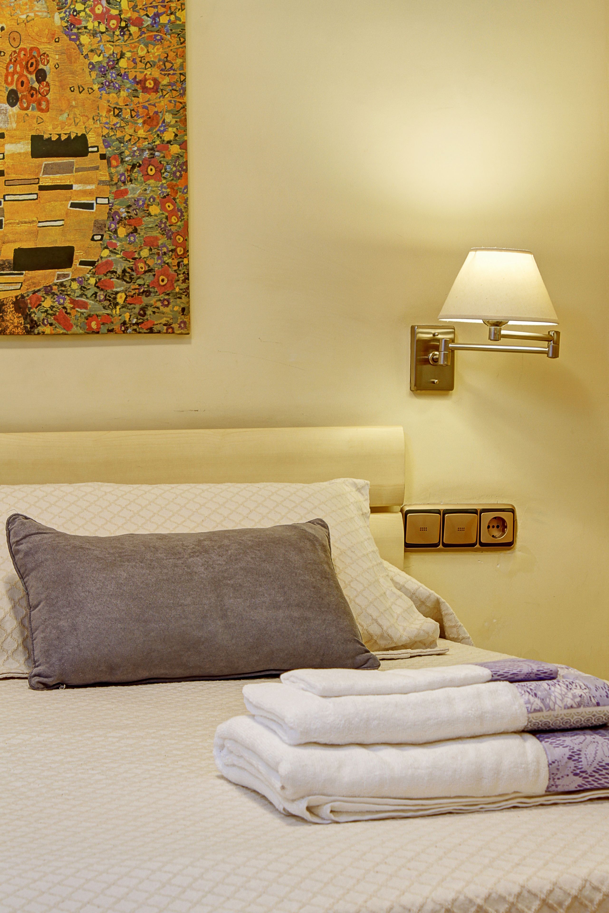 Une chambre d’hôtel avec un lit, une lampe fixée au mur et un tableau.