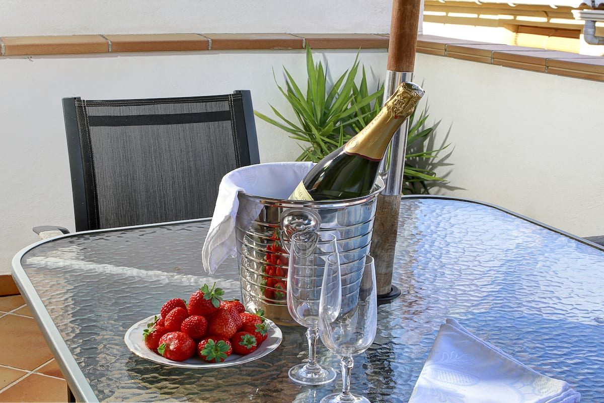 A glass table with a bottle of champagne, a plate of strawberries, and two empty wine glasses.