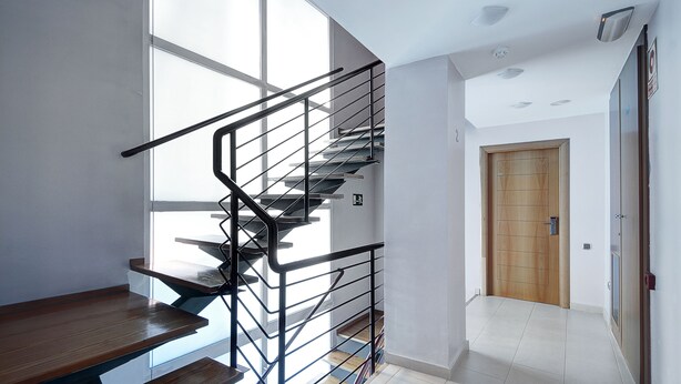 A modern staircase with metal railings, a wooden bench at the bottom, and a wooden door at the top. - Apartamentos Turísticos Centro (Granada)