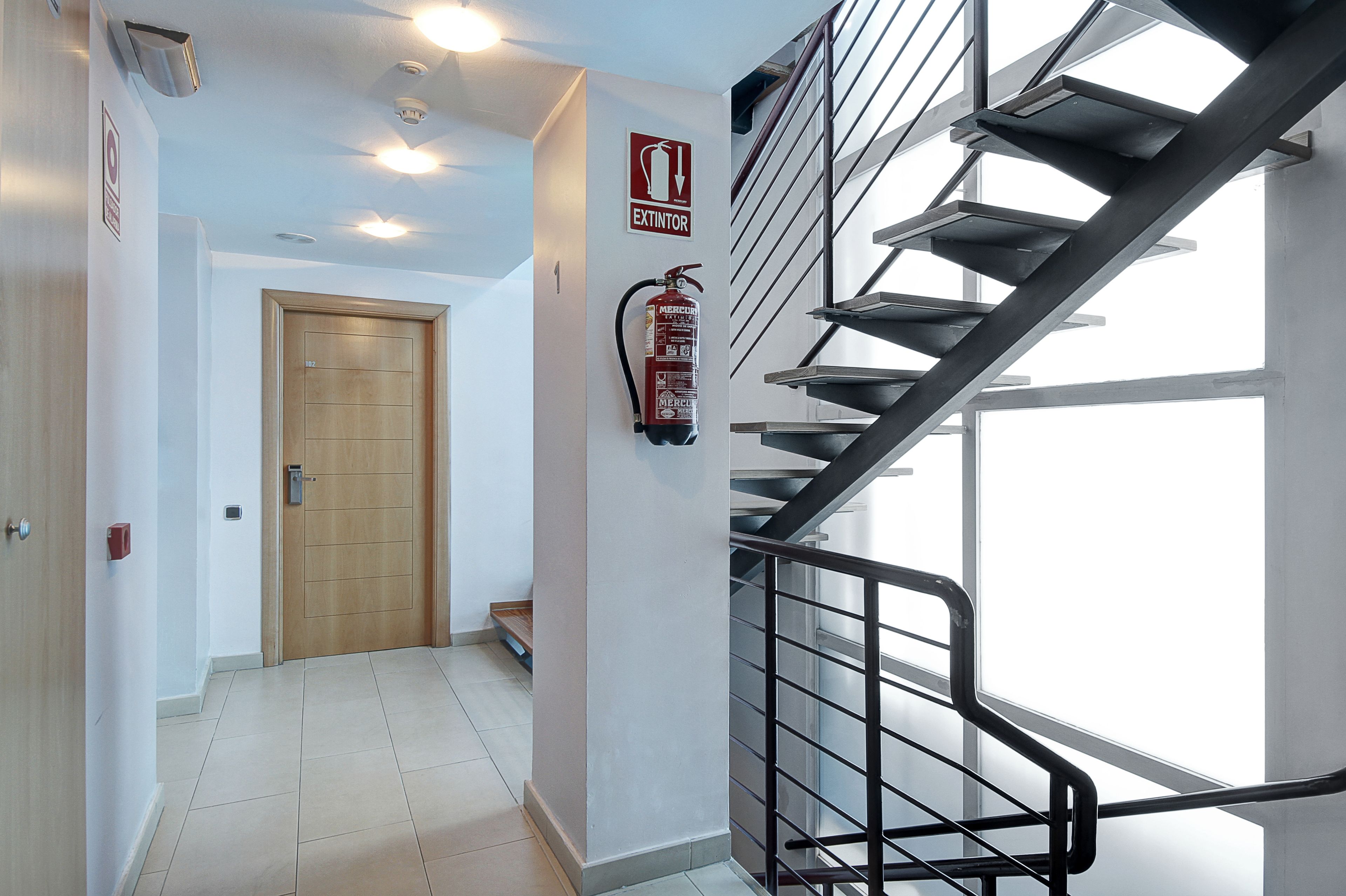 A modern interior with a wooden door, a fire extinguisher, and a metal staircase.