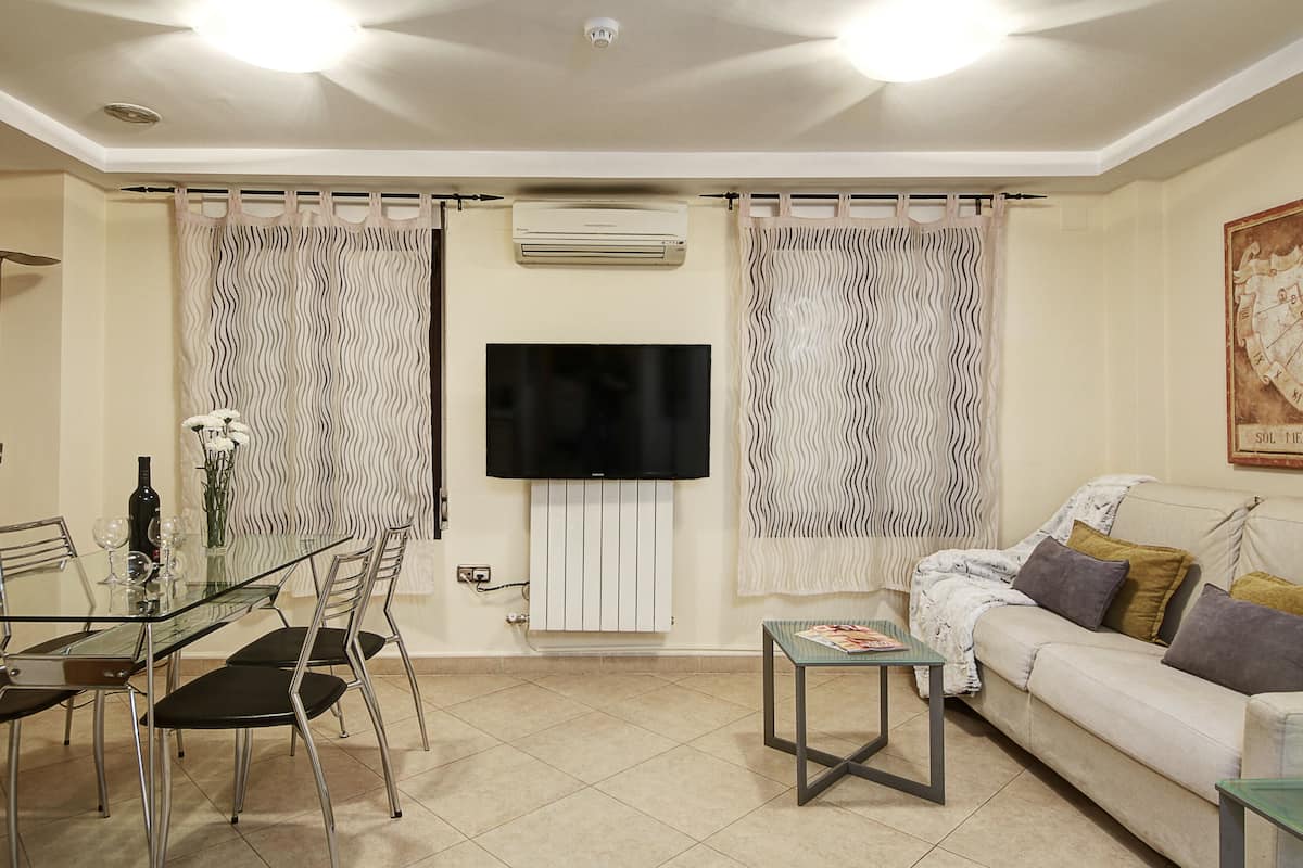 A living room with a glass dining table, chairs, a sofa, a television, and curtains.