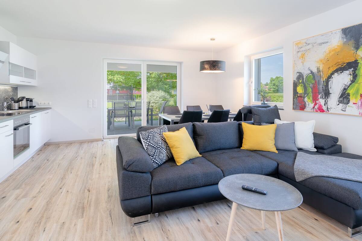 A modern living space with a sectional sofa, a small round table, and a kitchen area.
