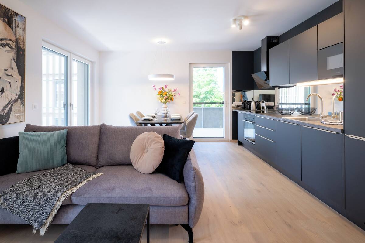 A modern living room with a grey sofa, a coffee table, and a dining area with a table and chairs.