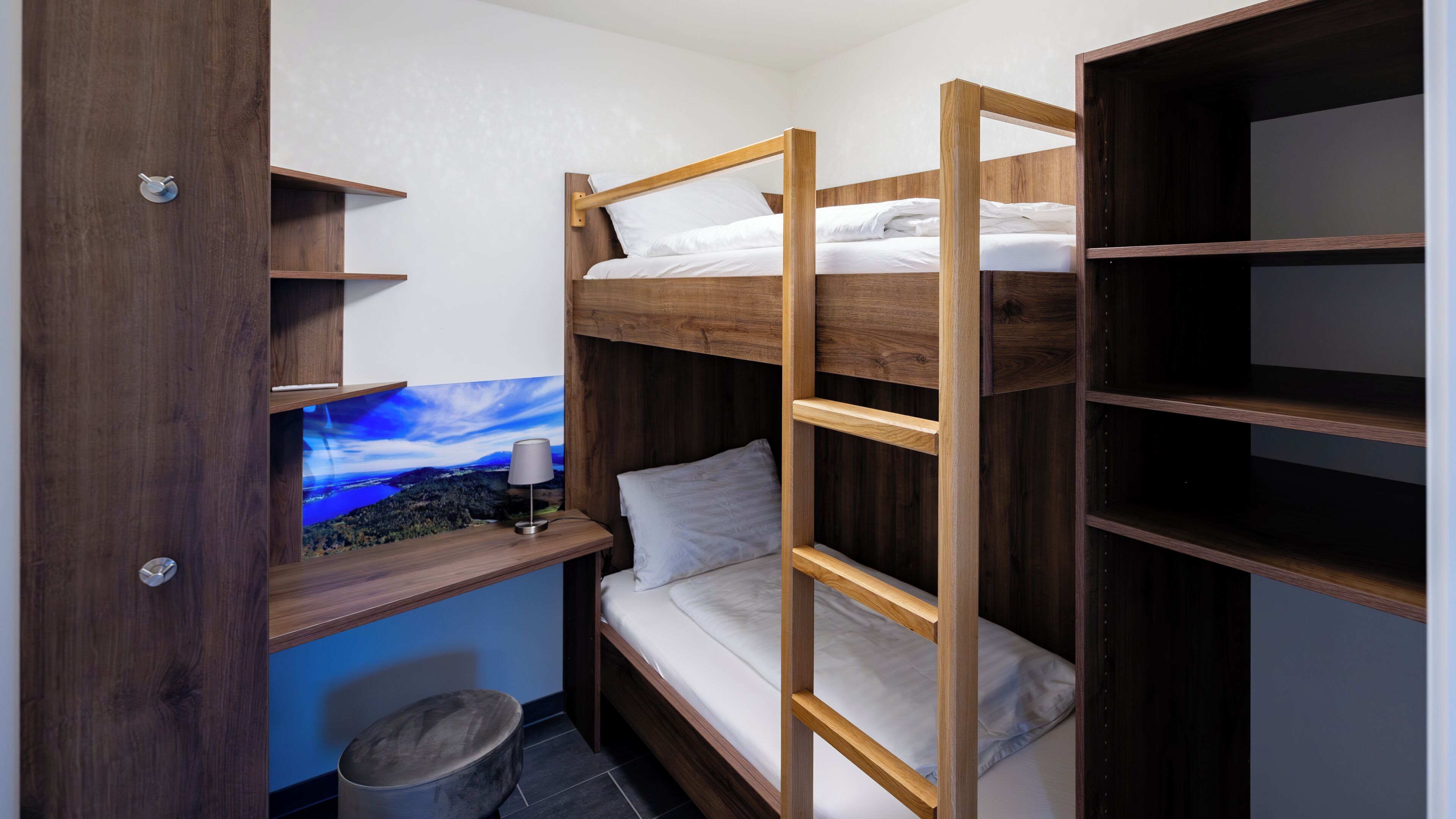 Une chambre avec un lit superposé à ossature en bois, un petit tabouret et une étagère fixée au mur.