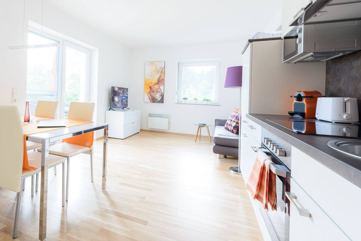 A modern kitchen with a dining area, featuring a wooden floor, white cabinetry, and a built-in oven.