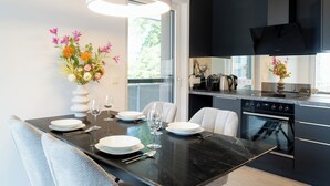A modern kitchen with a dining area, featuring a black countertop, white plates, wine glasses, and a vase with flowers. - Apartments Jesse (Sankt Kanzian am Klopeiner See)