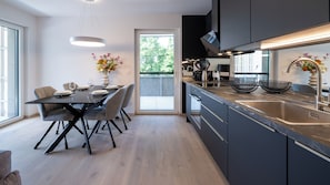 A modern kitchen with a dining area, large windows, and a view of greenery.