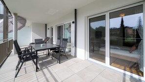 Eine moderne Terrasse mit Tisch und Stühlen, großen Schiebeglastüren und Blick ins Grüne.