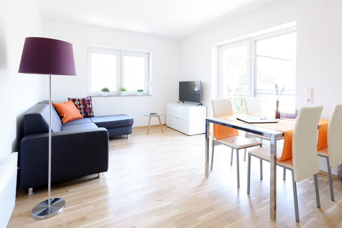 A modern living room with a sofa, a coffee table, a floor lamp, and a dining area with chairs and a table.