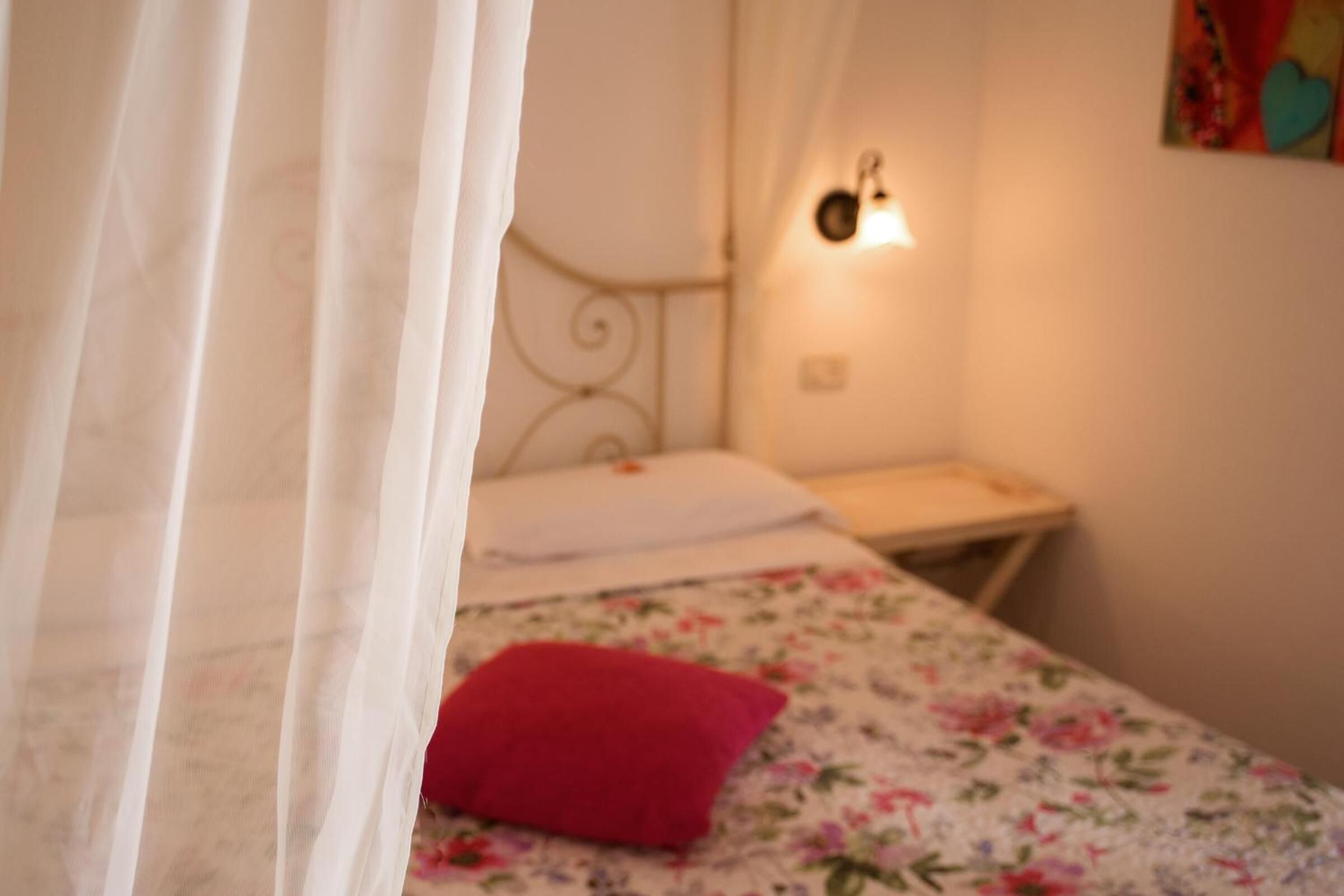 Une chambre à coucher avec un lit, un oreiller rouge, une table de chevet et une lampe fixée au mur.