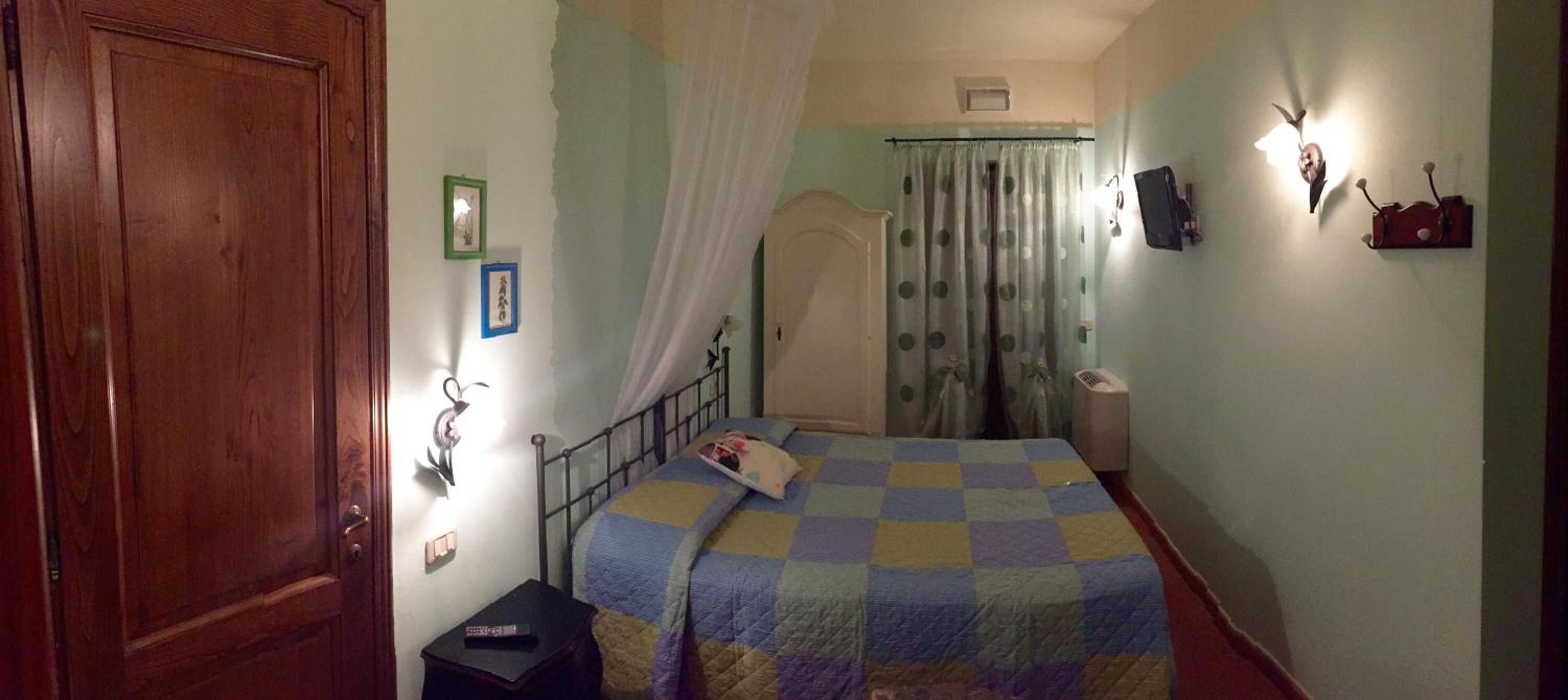 A bedroom with a bed, a wooden door, a nightstand, a wall-mounted shelf, and a curtain.