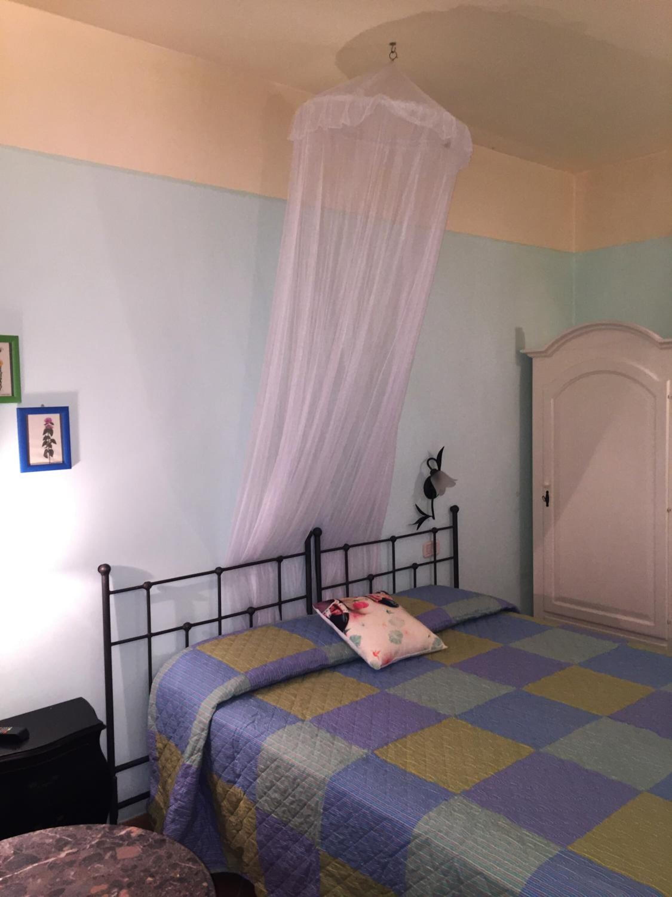 Un dormitorio con cama, mesita de noche, armario y mosquitero colgado.