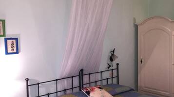 Un dormitorio con cama, mesita de noche, armario y mosquitero colgado.