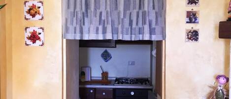 Una cocina con un reloj, una estufa a gas, un horno y una ventana pequeña con cortinas.