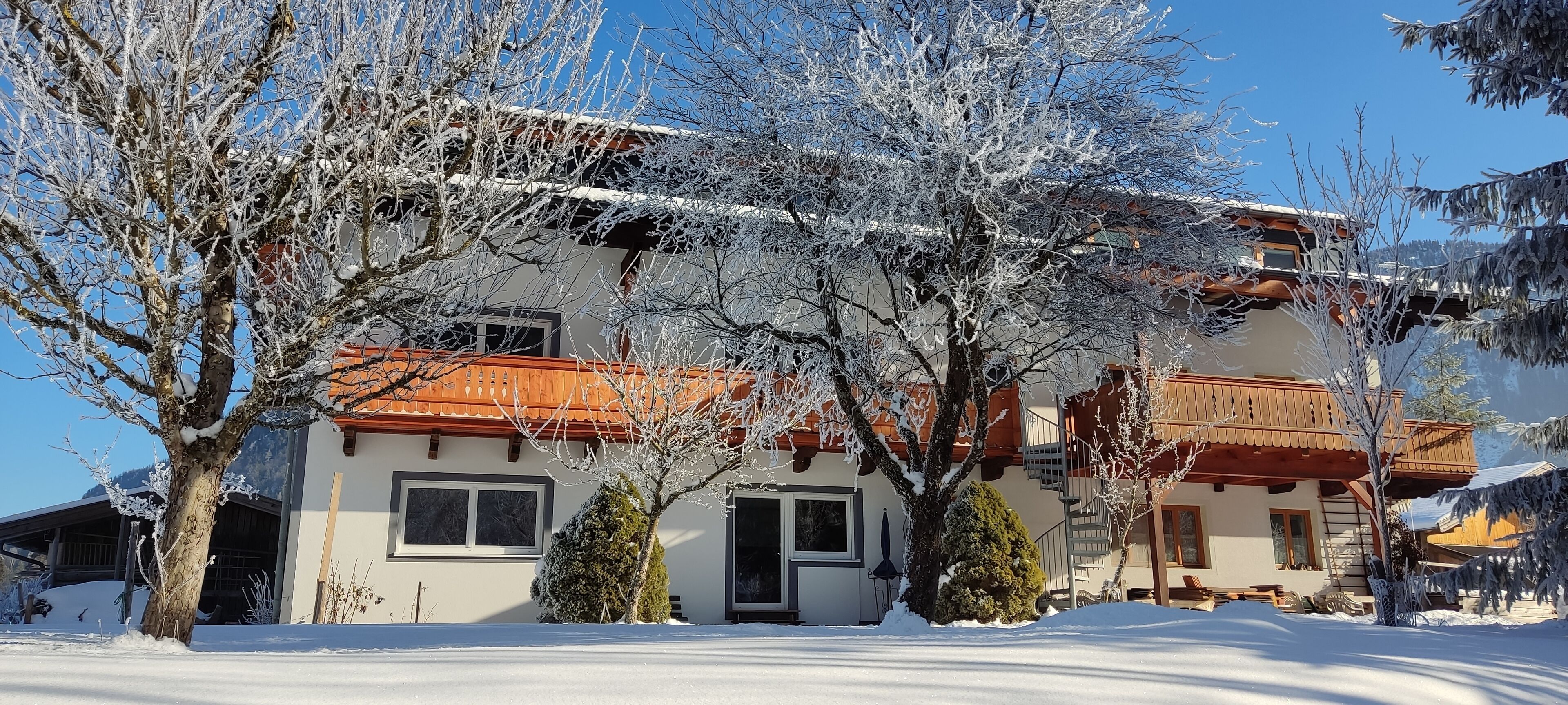 A snow-covered building with a red roof, multiple windows, and a balcony.