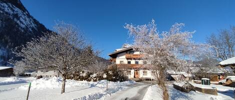 A snow-covered village with traditional wooden houses, a clear sky, and a mountain in the background.