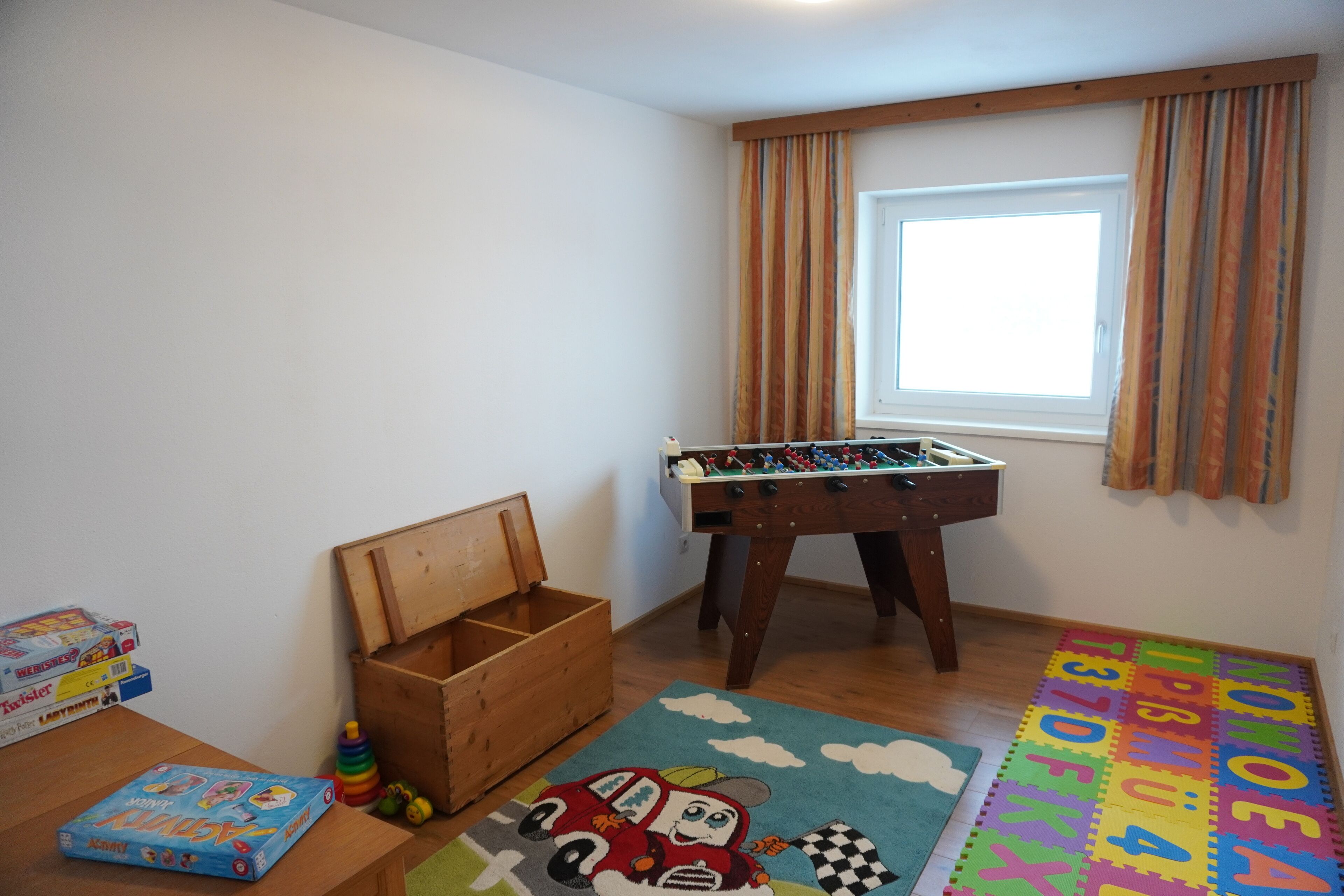 A child's playroom with a foosball table, alphabet foam mats, and toys.