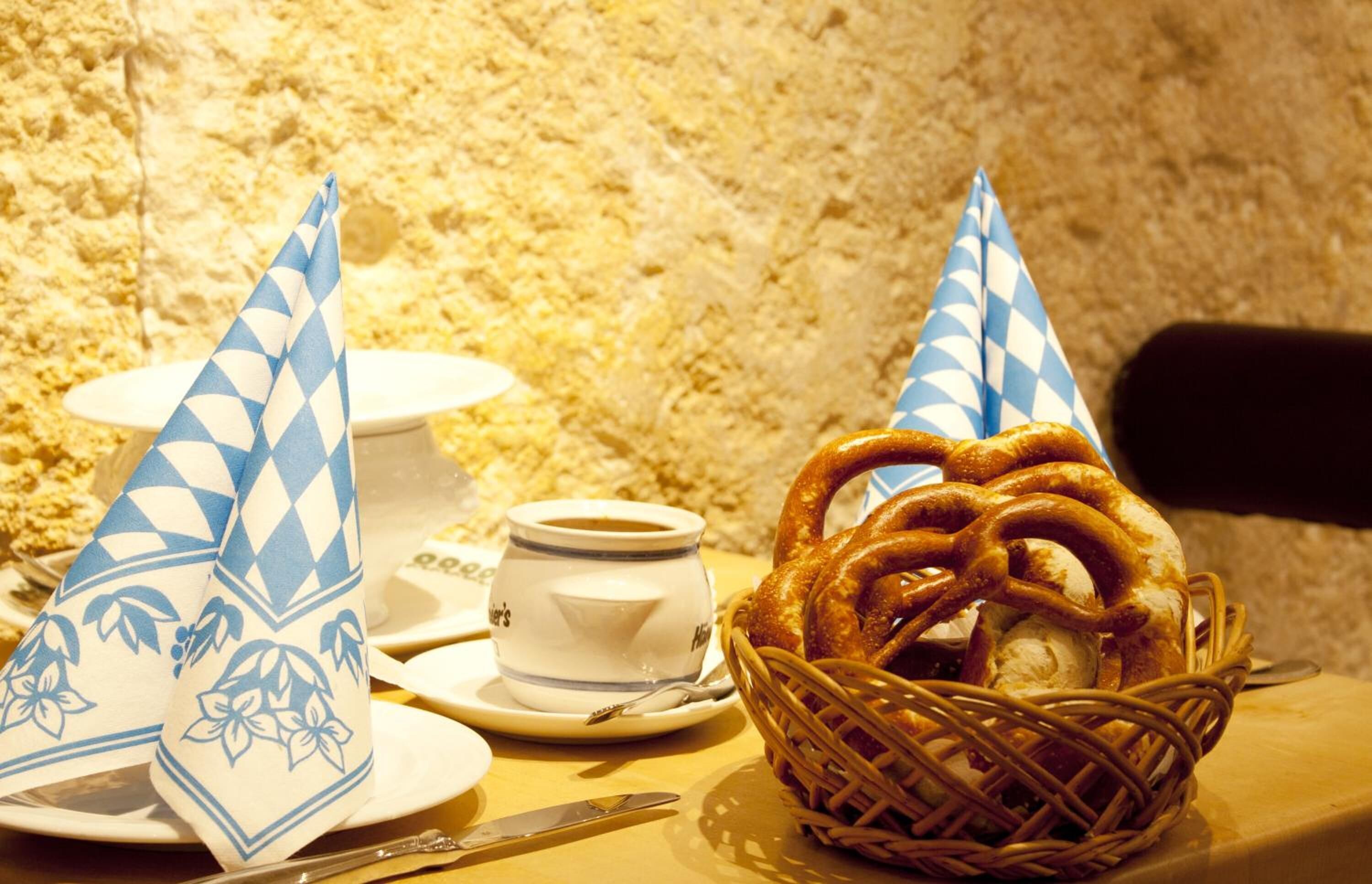 A table with a basket of pretzels, a cup of coffee, and a white teapot with a blue pattern.