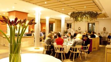 A restaurant with round tables and chairs, a central column, and a hanging plant.