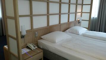 Habitación de hotel con cabecera de madera, teléfono en la mesita de noche y cama con ropa blanca bien tendida.
